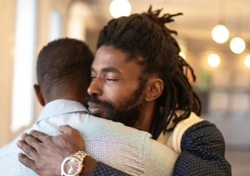 two men hugging, one with his face towards camera, one facing away