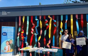 Three people standing next to the vaccination stall holding totebags.