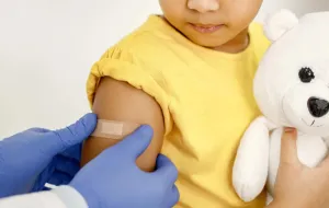 A child having a plaster put on. The child is holding a cuddly toy.