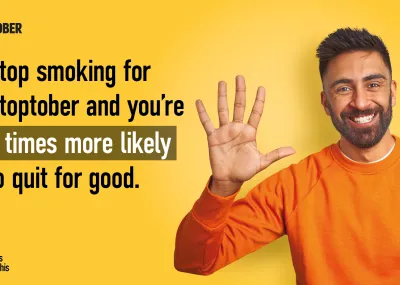 Man in orange jumper smiling with hand raised, text says 'stop smoking for stoptober and your 5 times more likely to quit for good'.