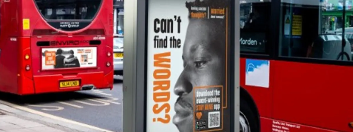 An on-street advertising display board featuring the stay alive campaign ('can't find the words?' + the side profile of a man's face), with two red London in the background