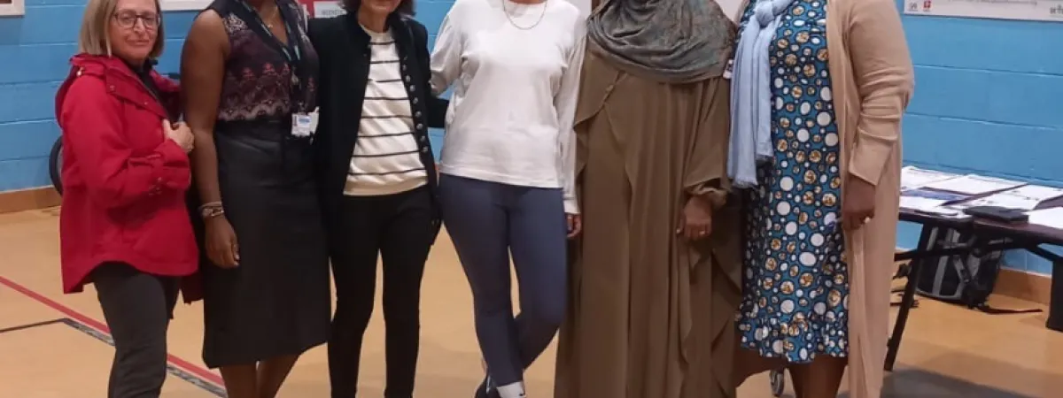 A group shot of 6 women in the gym, all stood together in a row and smiling to camera