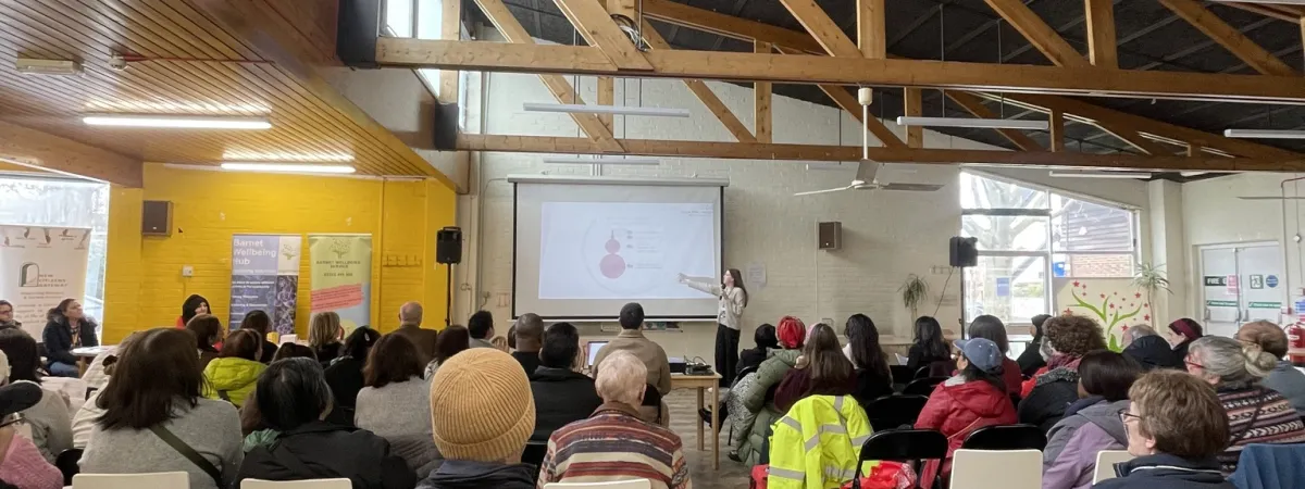 Picture of group listening to a female speaker delivering a presentation.