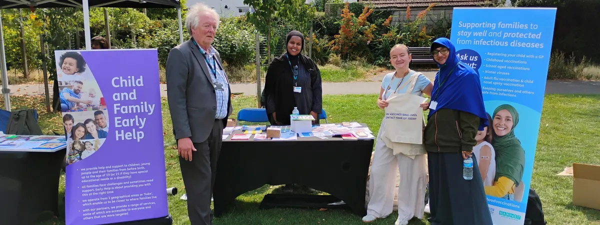 People infront of a stand displaying information about childhood vaccinations.