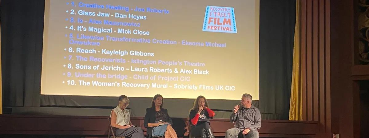 Four people sat on a stage in front of a cinema screen
