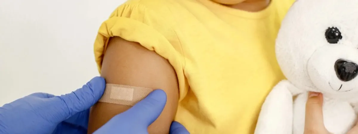 A child having a plaster put on. The child is holding a cuddly toy.